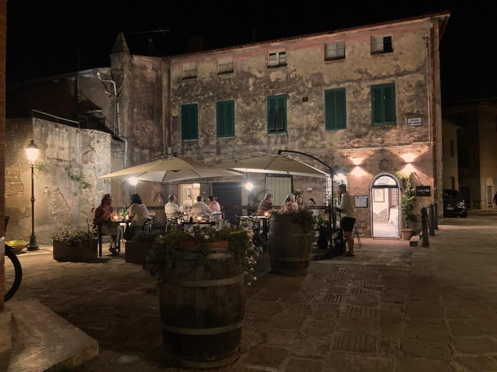 Terrasse der Osteria 1935 in Giuncarico in der Toskana am Abend mit stimmungsvoller Beleuchtung und Gästen, die Im Restaurant an Tischen sitzen und essen.